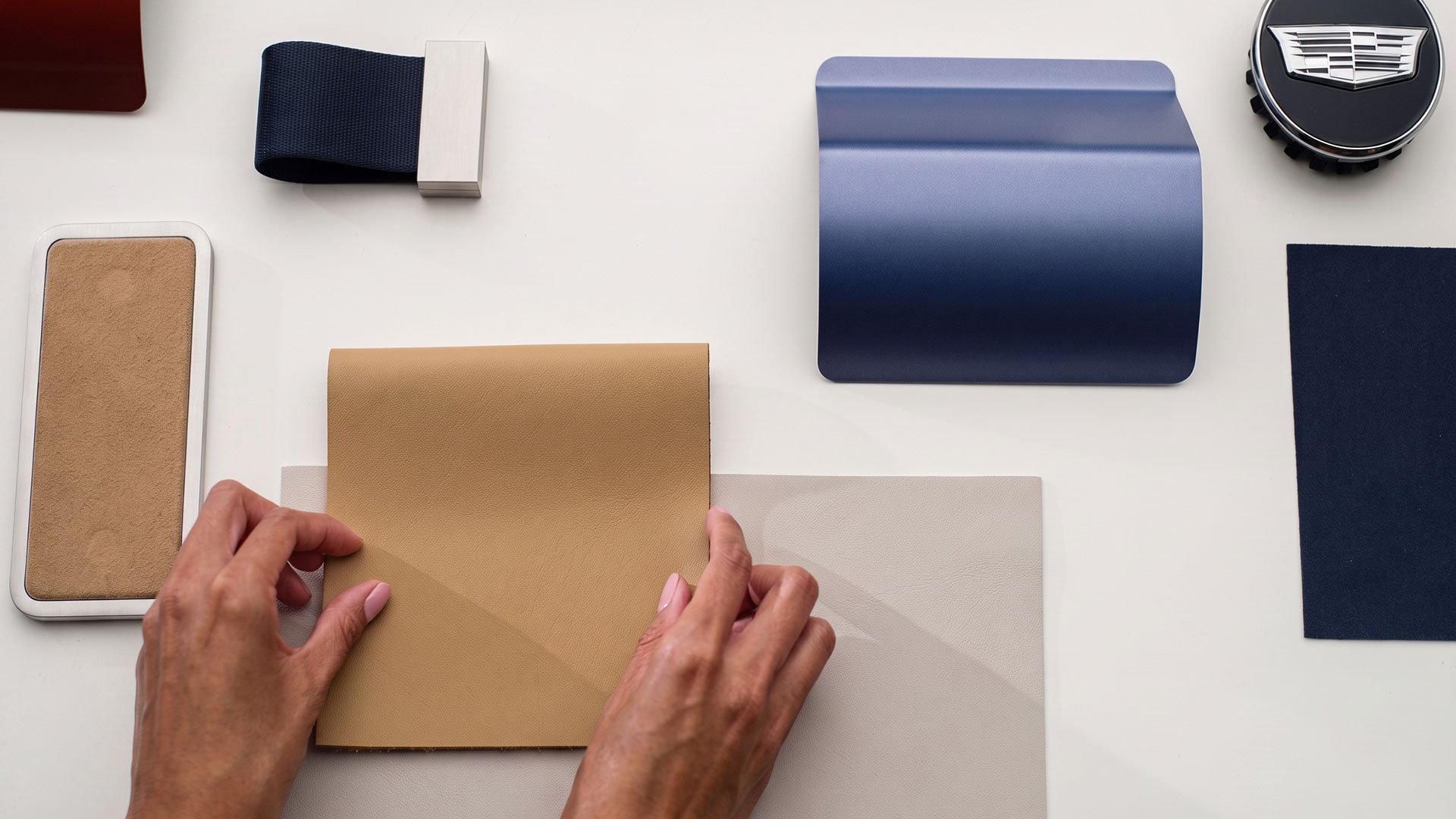 Unas manos acomodan muestras de material de color Beige en una mesa Blanca, rodeadas de muestras de diseño de interiores y de colores.