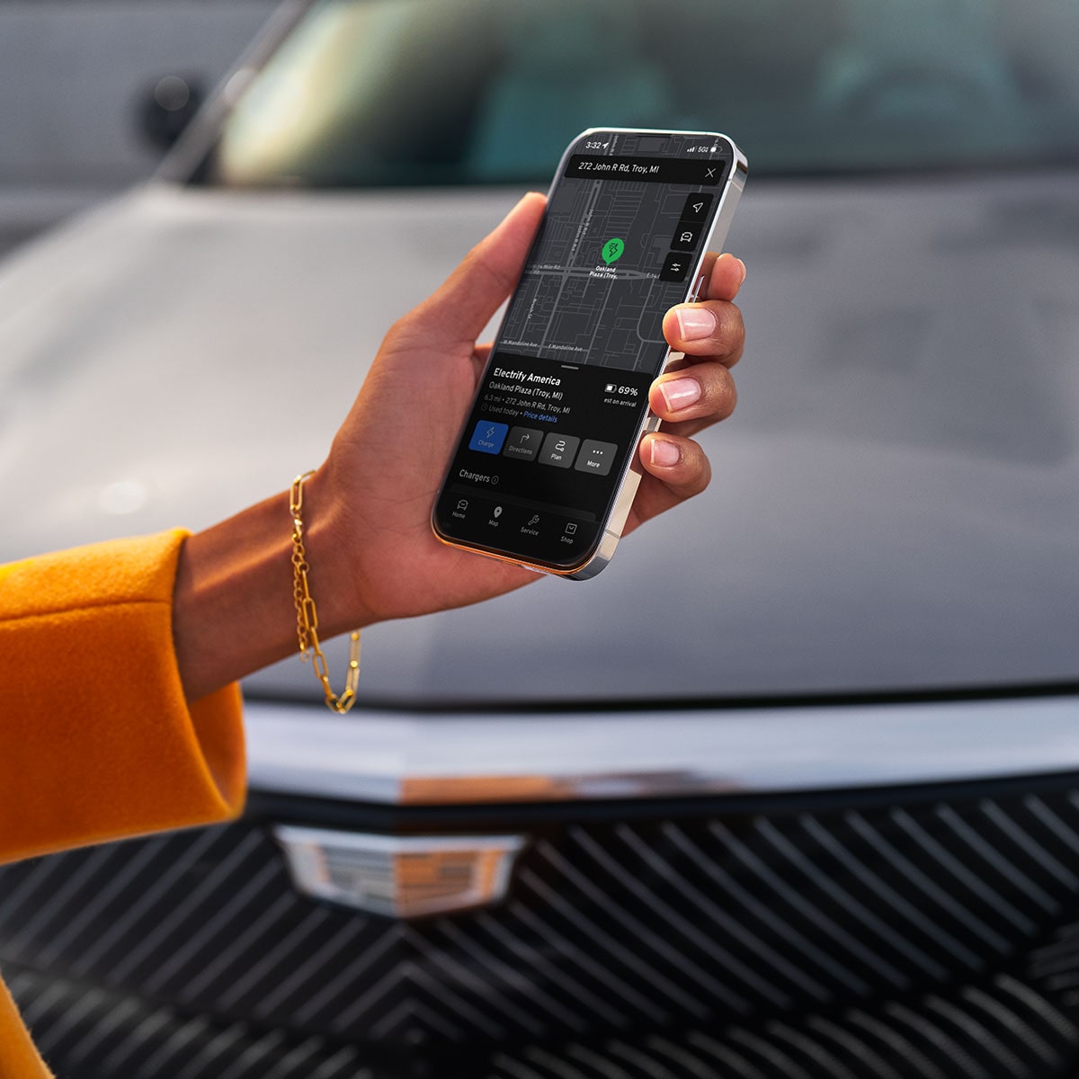 Hand Holding a Smartphone Displaying Vehicle Controls in Front of a 2027 Cadillac LYRIQ-V.
