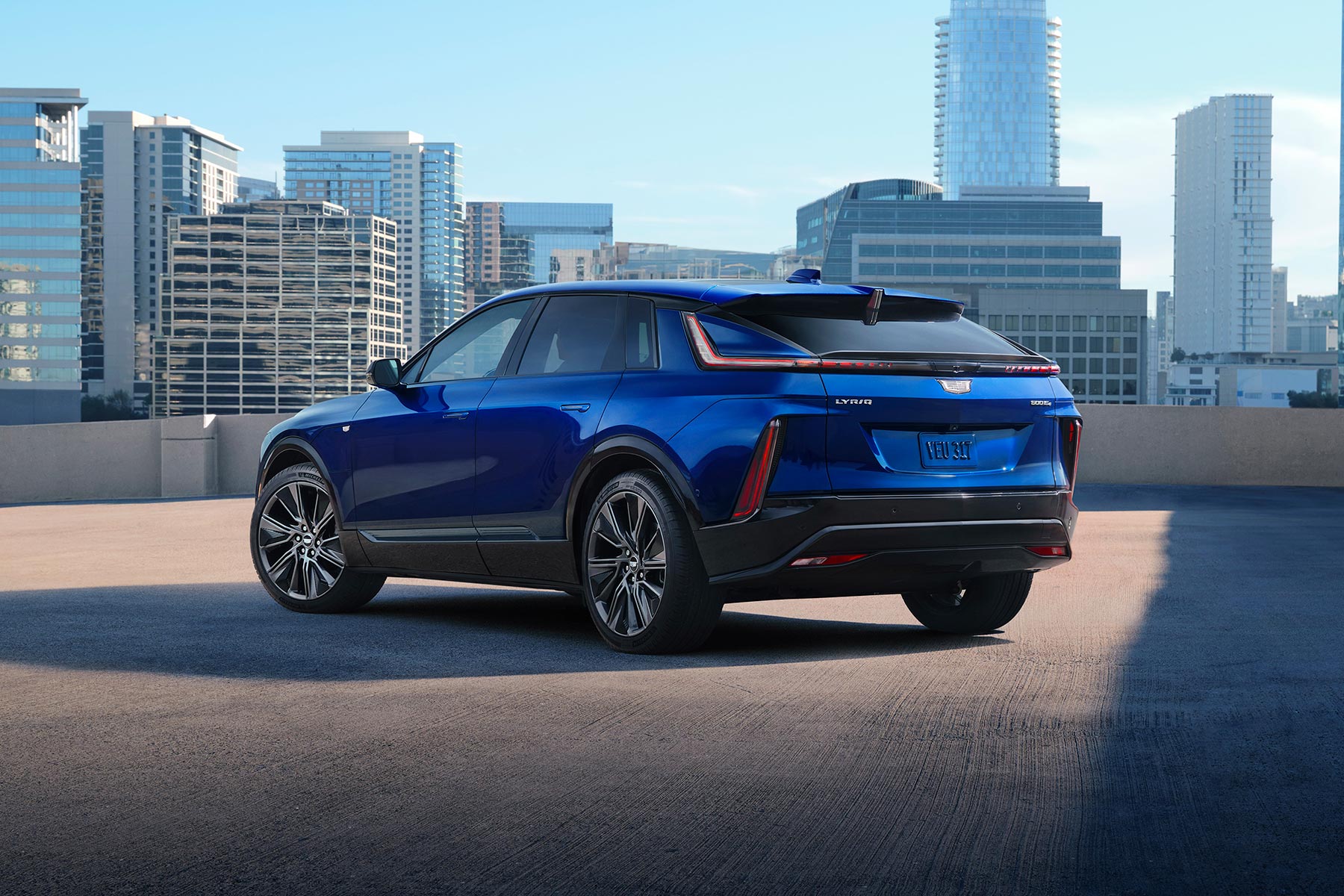 Blue 2027 Cadillac LYRIQ Parked on a Rooftop With a City Skyline in the Background.