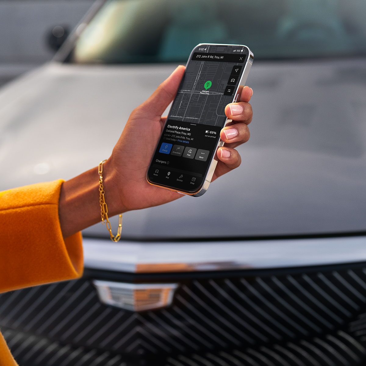 Hand Holding a Smartphone Displaying Cadillac Vehicle Controls in Front of a 2027 Cadillac LYRIQ-V