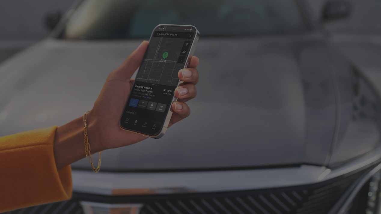 Hand Holding a Smartphone Displaying the myCadillac Mobile App Near a 2027 Cadillac LYRIQ.
