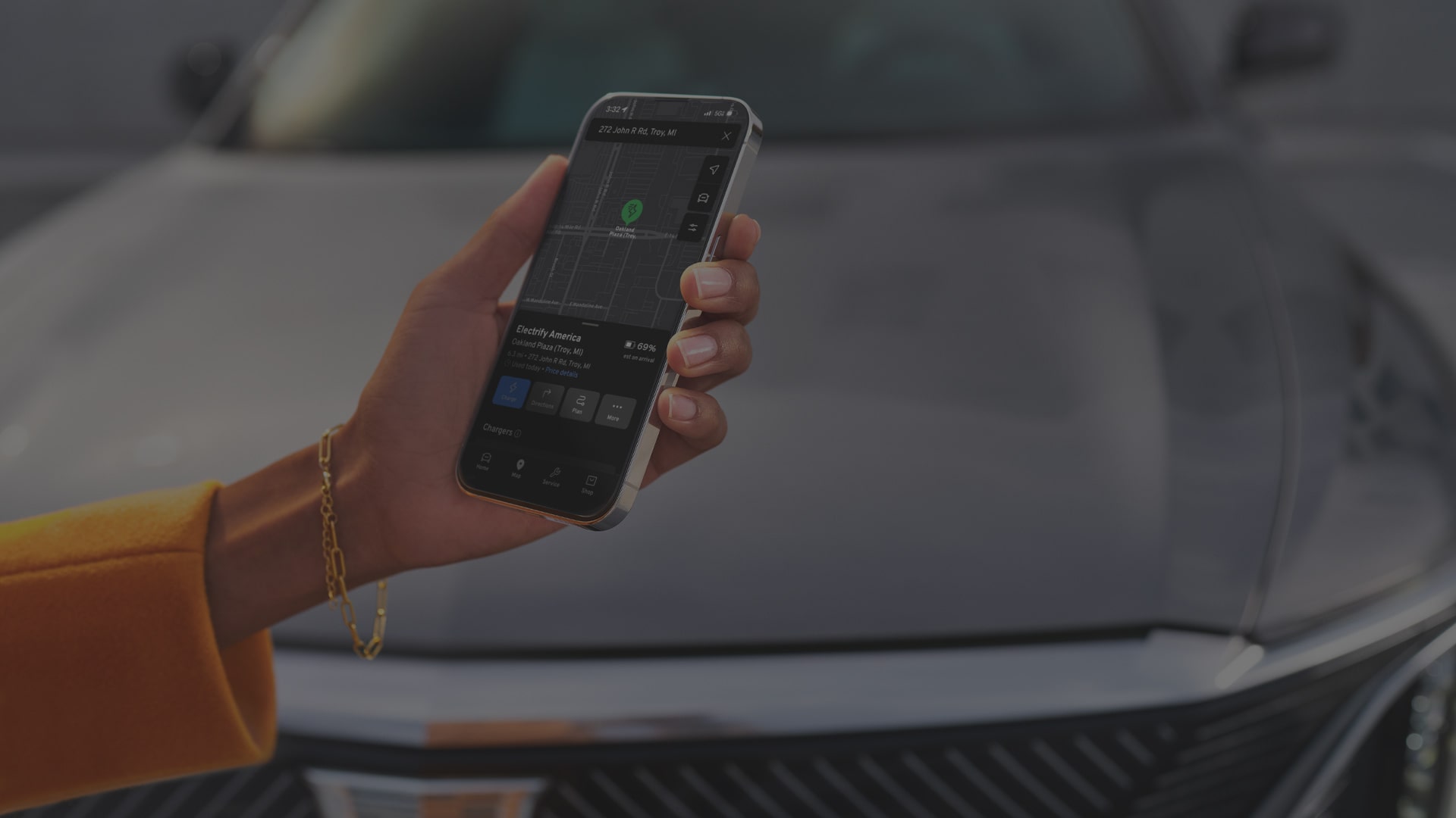 Hand Holding a Smartphone Displaying the myCadillac Mobile App Near a 2027 Cadillac LYRIQ.