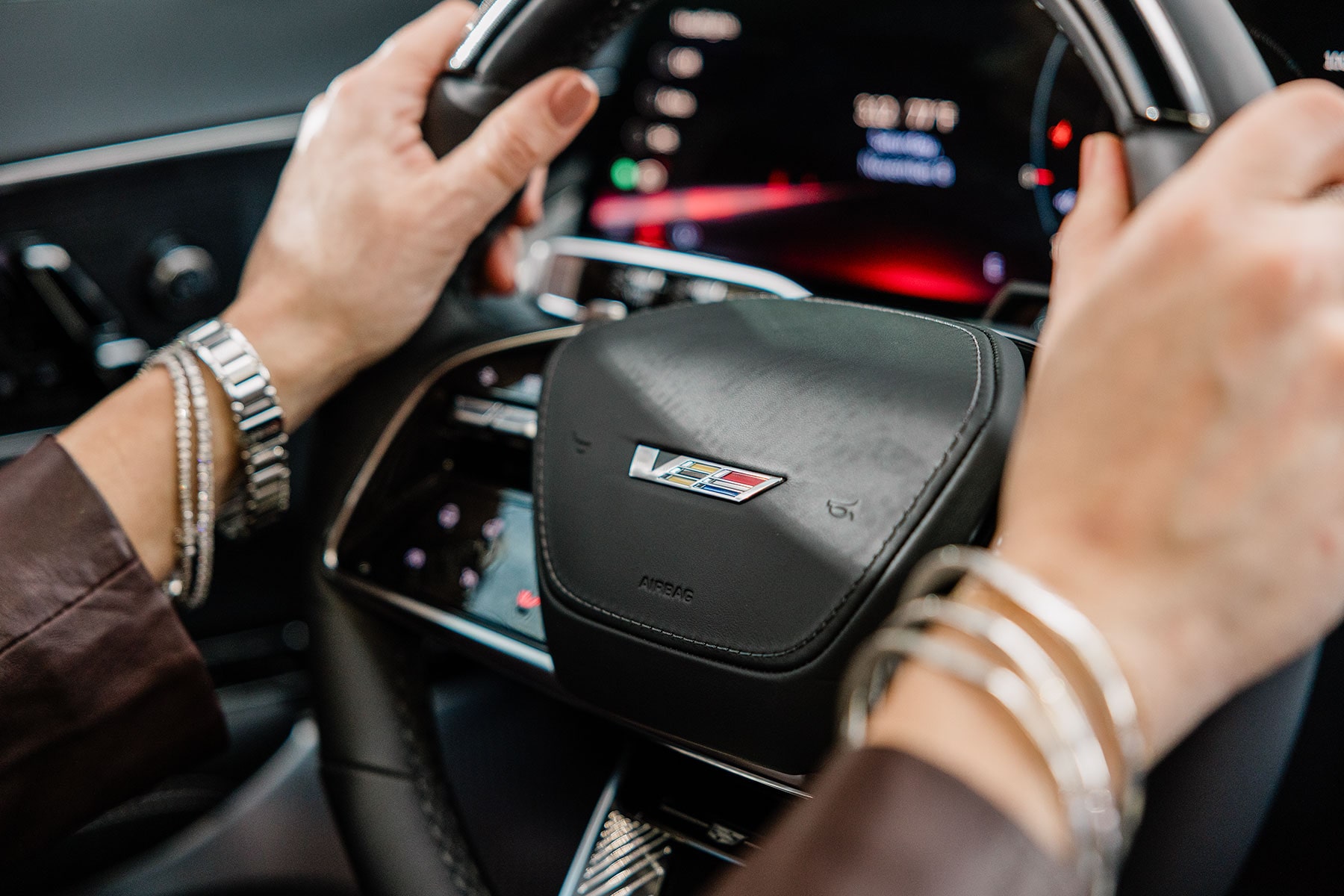 Hands on the Steering Wheel of a 2027 Cadillac LYRIQ-V With a Digital Instrument Display.