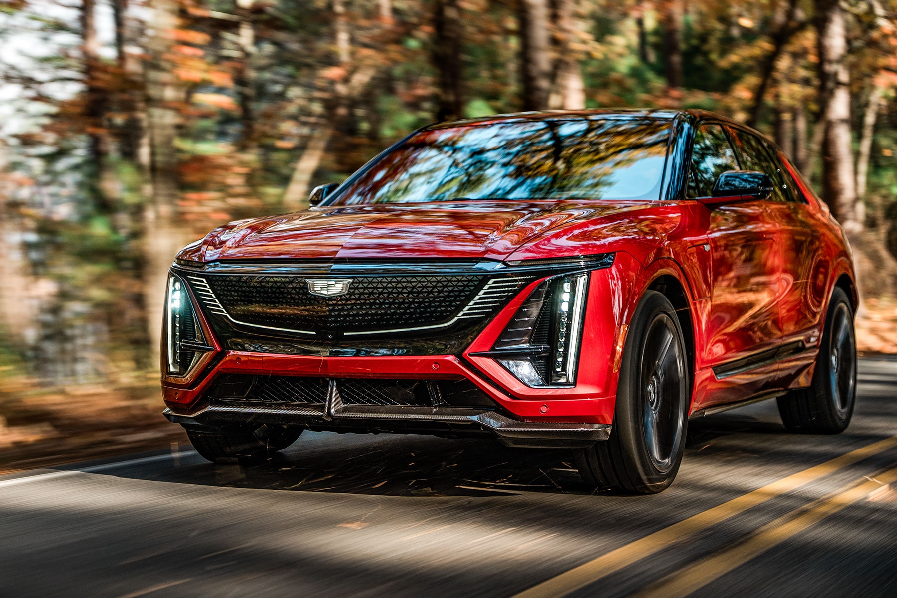 Red 2027 Cadillac LYRIQ-V Driving on a Tree-Lined Road.