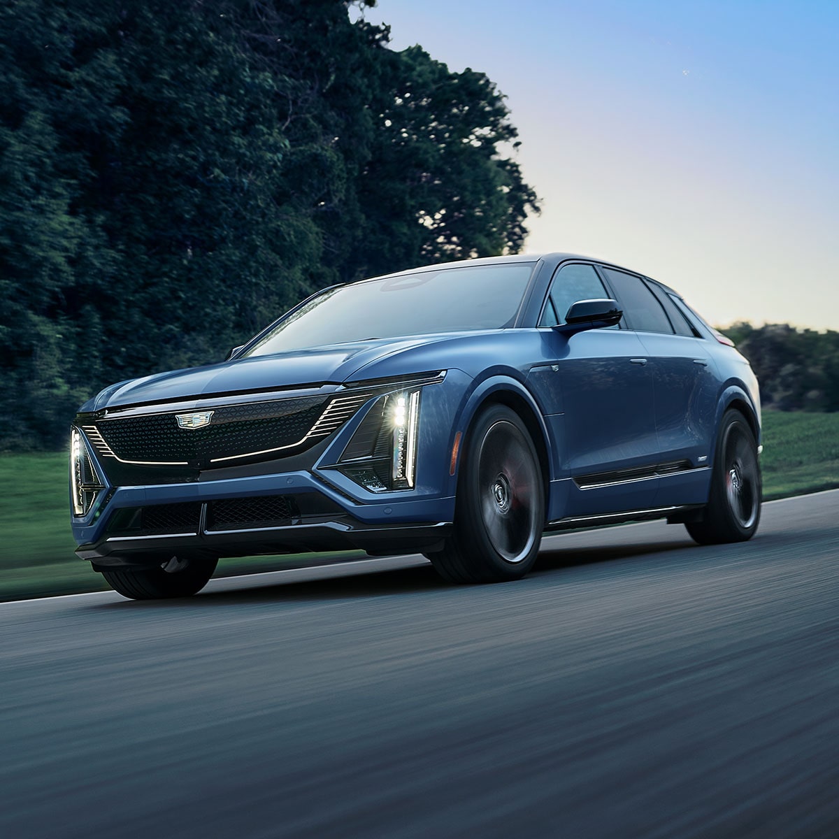 Blue 2027 Cadillac LYRIQ-V Driving on a Road With Illuminated LED Signature Lighting.