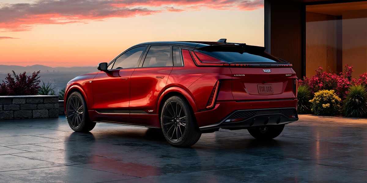 Rear Three-Quarter View of a Red 2027 Cadillac LYRIQ-V Parked Outside a Modern Home at Sunset.