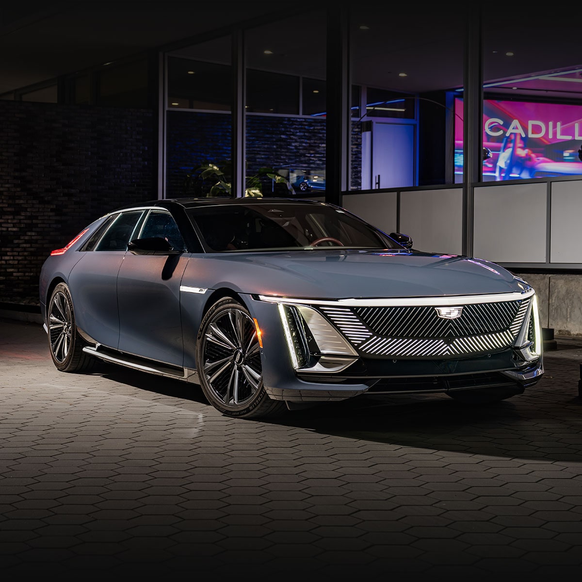 A Front-Side View of a Dark Blue Cadillac CELESTIQ Luxury Electric Vehicle Parked at Night in Front of a Building with a 'Cadillac' Sign.