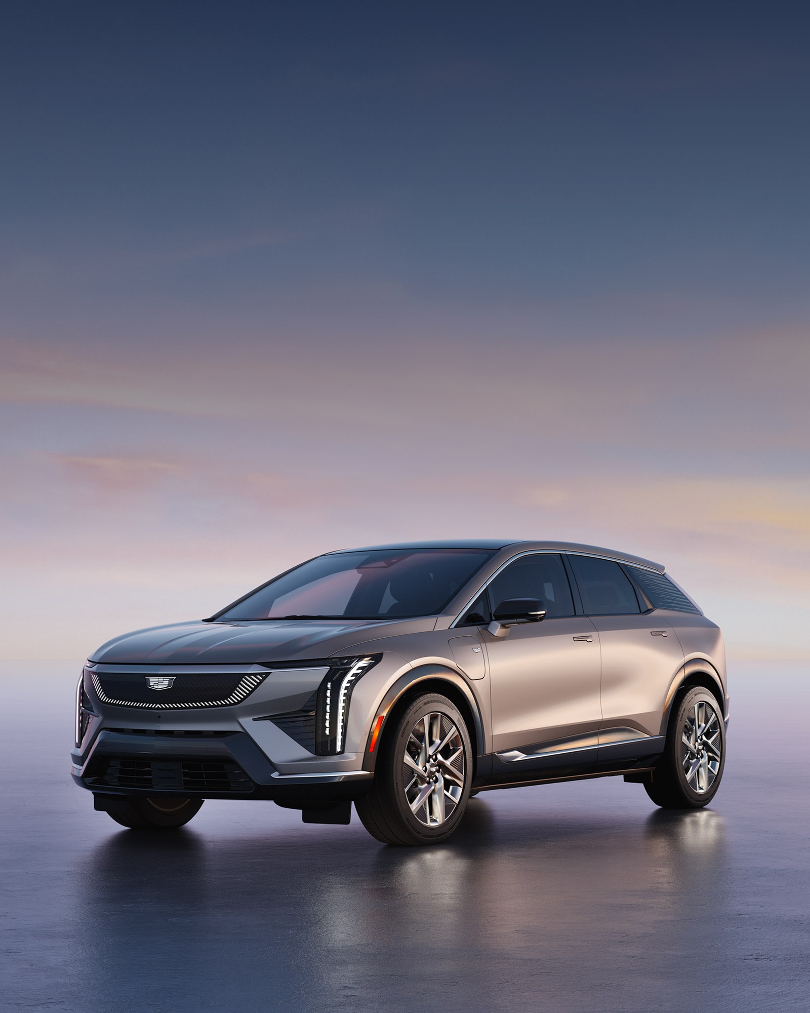 Three-quarters View of a Silver Cadillac OPTIQ Electric SUV Parked on a Smooth, Reflective Surface at Dusk