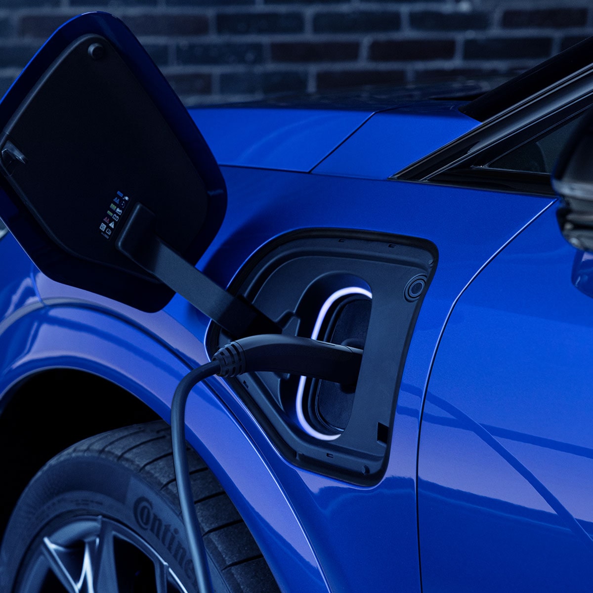 Close-up of Red Cadillac OPTIQ charging, with a charging cable plugged into an illuminated charging port.
