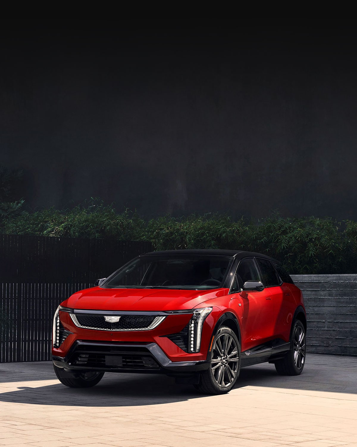 Three-quarter View of a Red Cadillac OPTIQ Parked by a Brick Wall and Green Shrub