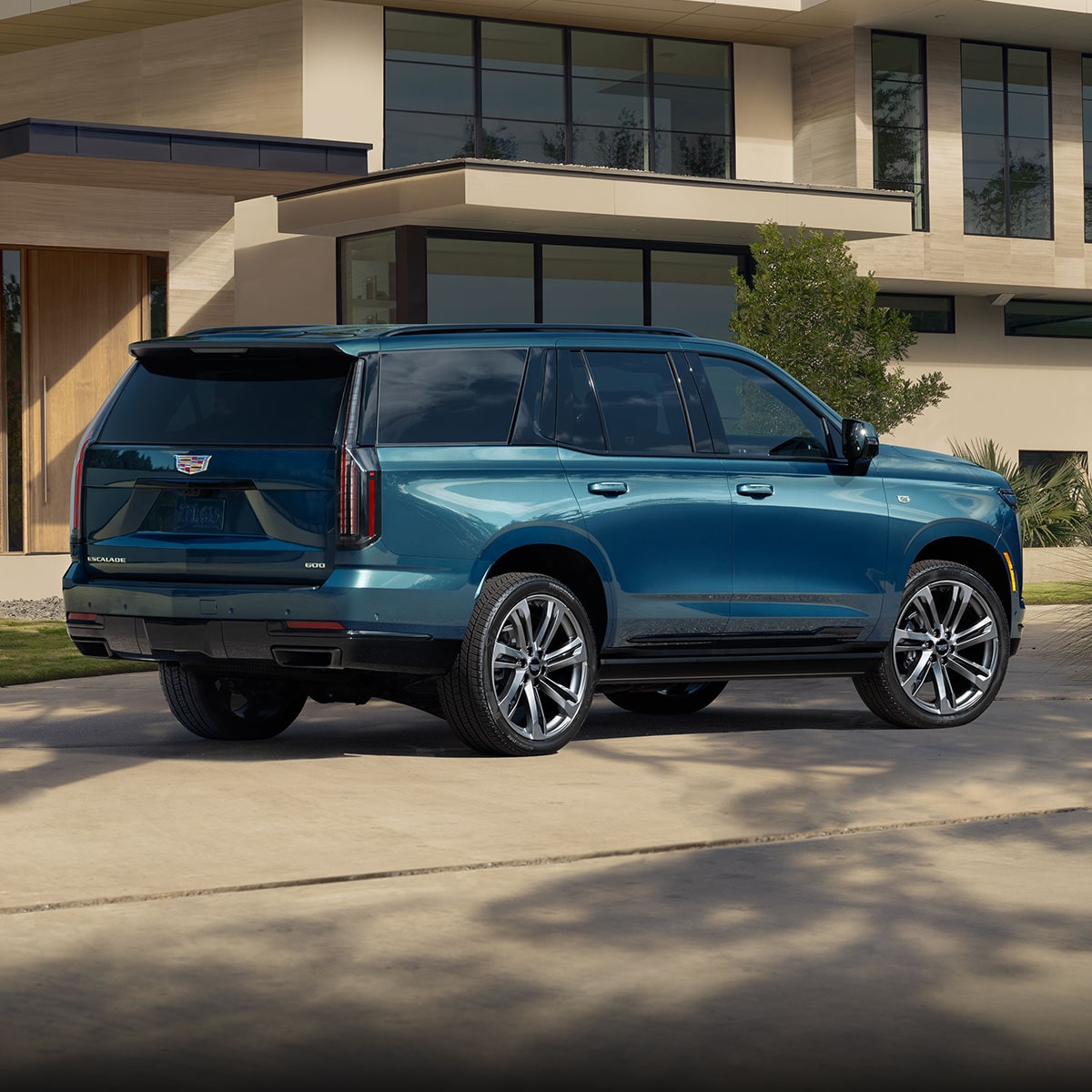 A Rear Passenger Side View of a Dark Blue Cadillac SUV Parked on a Paved Driveway in Front of a Modern House