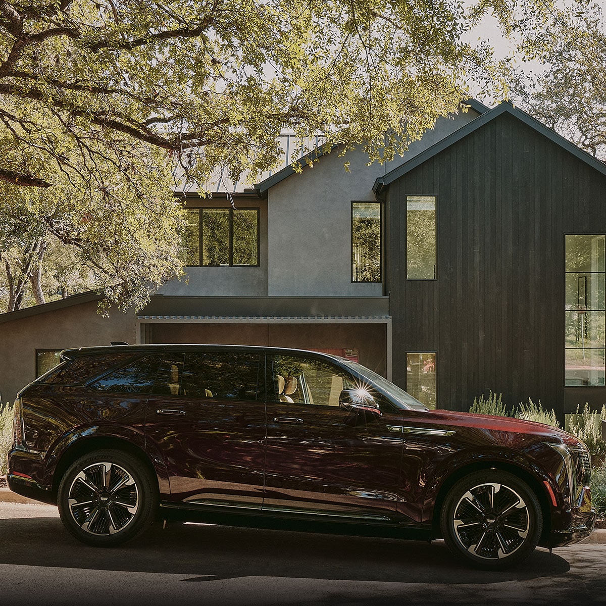 A Side Profile of a Dark Red Cadillac SUV Parked on a Driveway with a Man Walking Away in the Foreground and a House behind