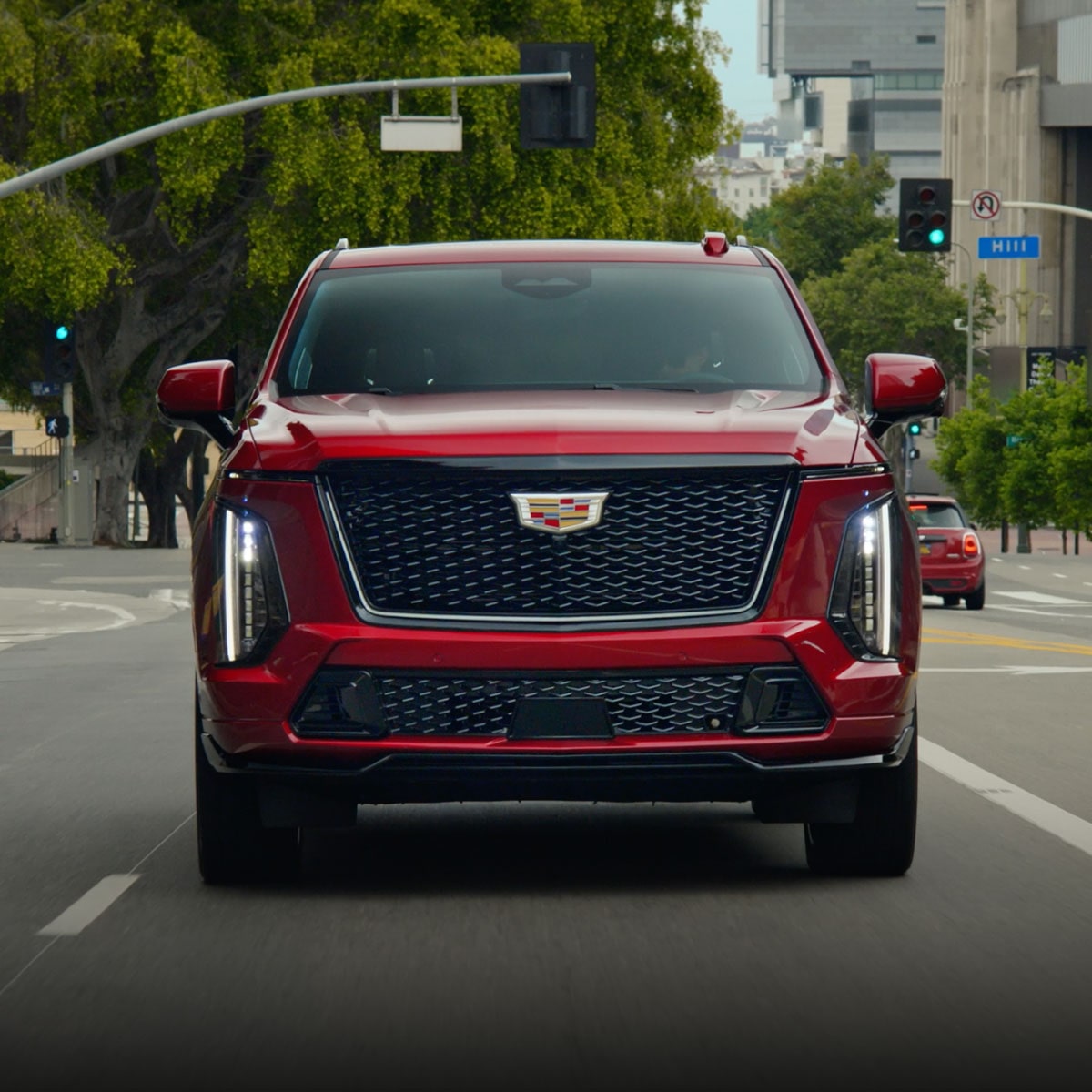 A Red Cadillac Escalade V-Series SUV on a City Street with Trees and Traffic Lights