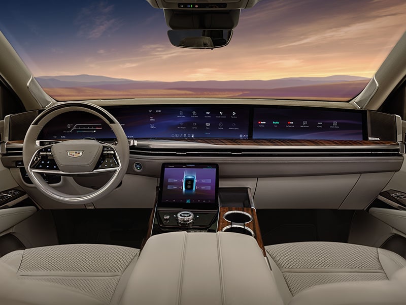 An Interior Dashboard View of a Cadillac with Wide Screens Displaying Various Controls and Information and a Mountain Landscape through the Windshield
