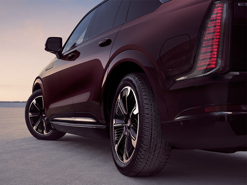 A Rear Passenger Side View of a Dark Red Cadillac SUV's Wheel and Tire on a Paved Surface at Sunset
