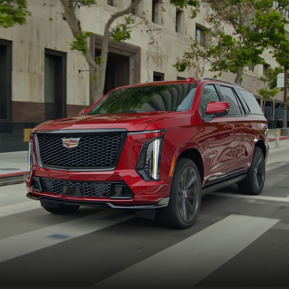 A Red Cadillac Escalade SUV Driving through a City Street with Modern Buildings