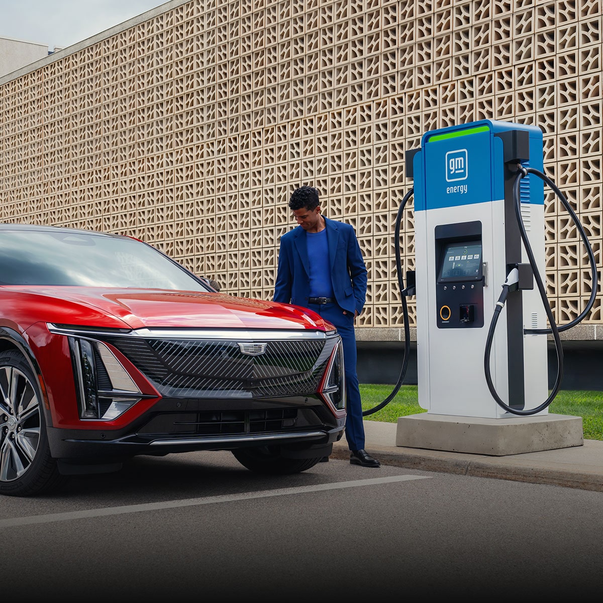 A Man in a Blue Suit Standing by a Red Cadillac OPTIQ Parked at a GM EVgo charging station