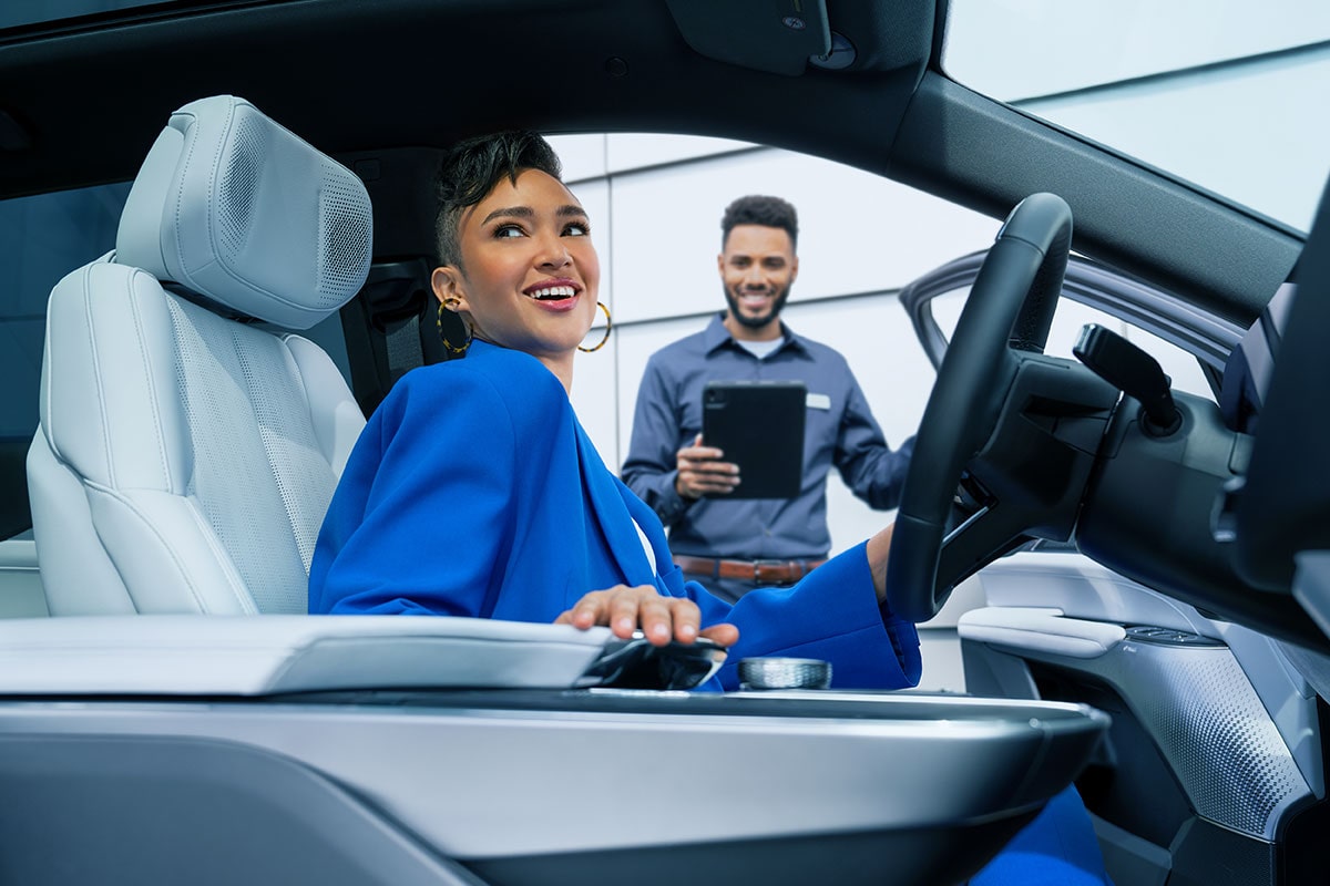 A Smiling Cadillac Customer Sitting in Her Vehicle with a Certified Service Technician Nearby