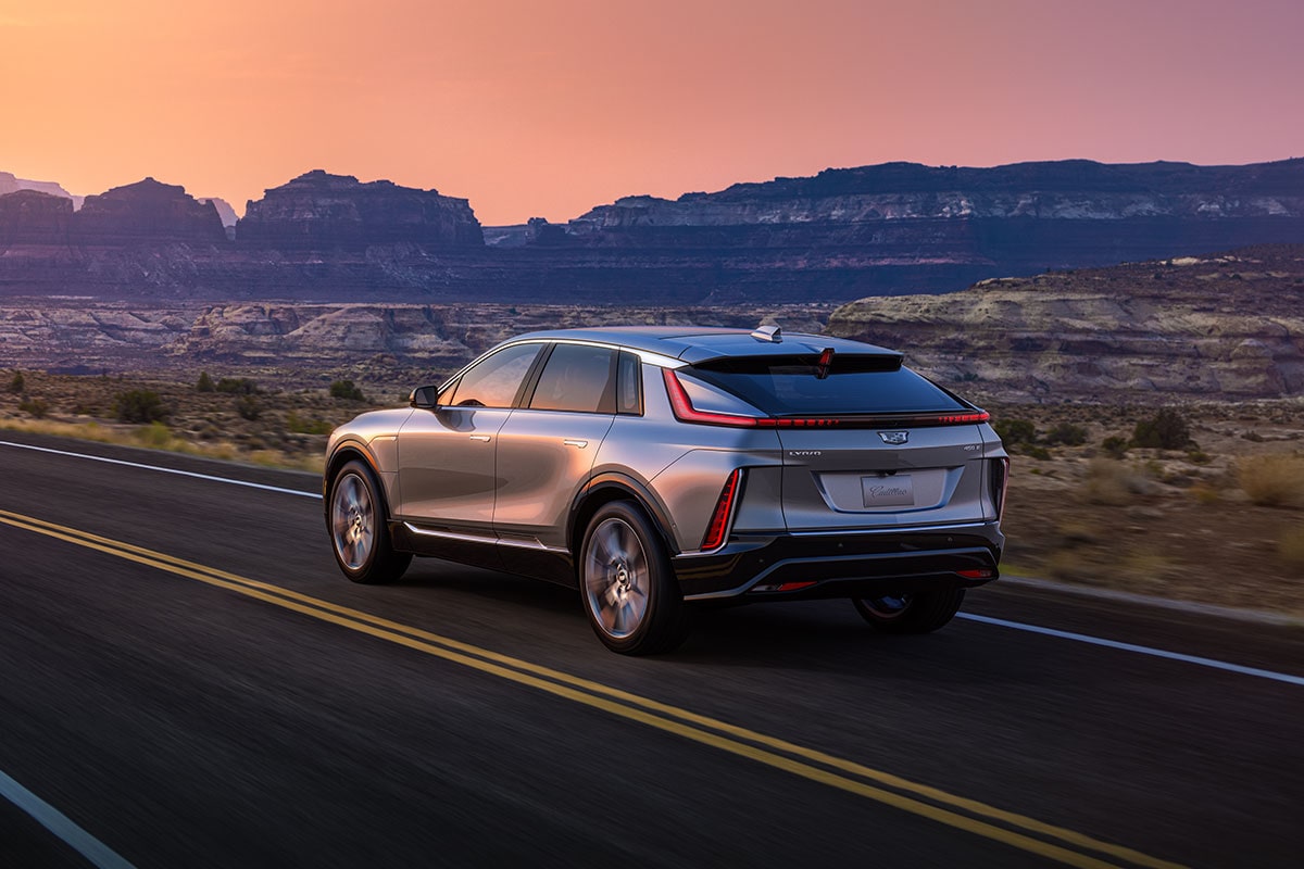 Rear View of a Gray Cadillac LYRIQ Driving Down an Open Road in the Desert During a Sunset