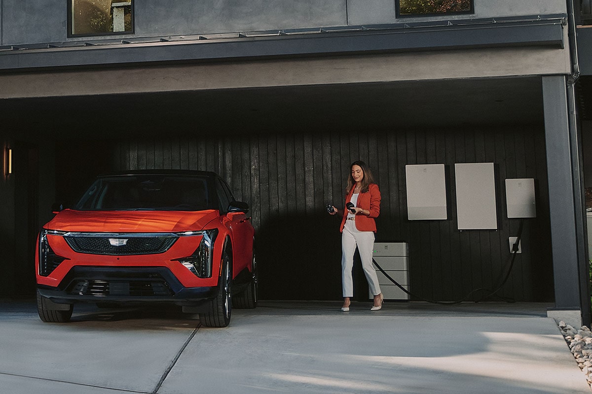 A Business Woman with a GM Energy Home Charger Walking Towards a Red OPTIQ Outside of a Modern Building