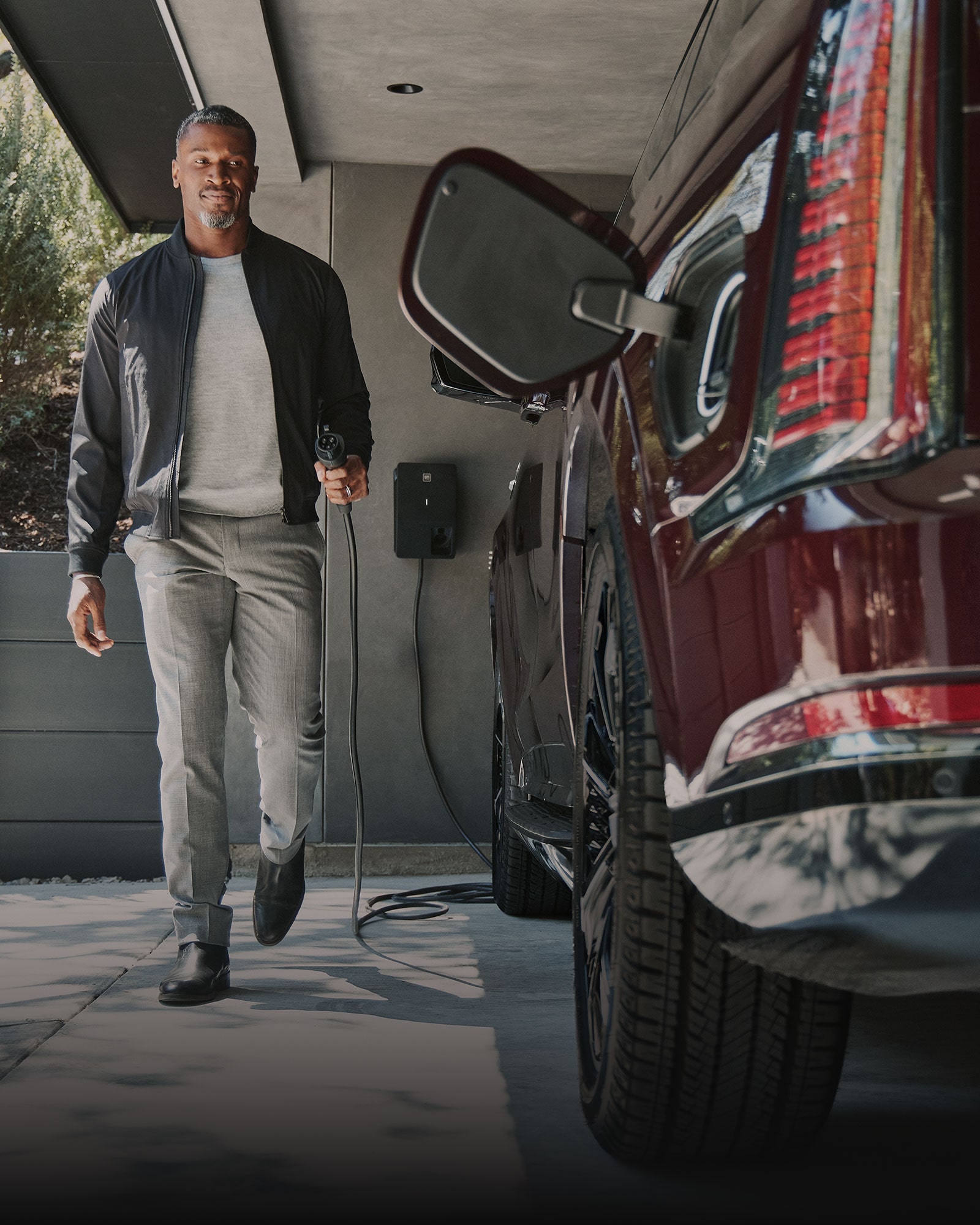 A Man with a GM Energy Charger Walking Towards a Cadillac EV's Charging Port in a Garage