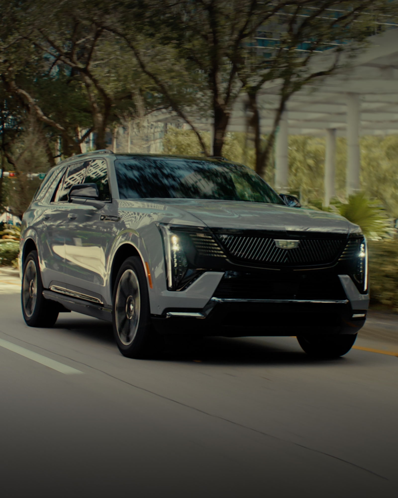 Three-quarter View of a Cadillac ESCALADE IQL Driving Through a City Street Lined with Trees