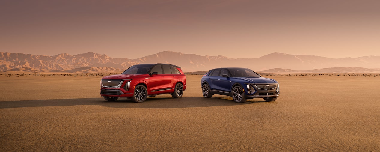 A Red Cadillac LYRIQ Parked Next to a Dark Blue Cadillac VISTIQ in the Open Desert Outlooking the Mountains