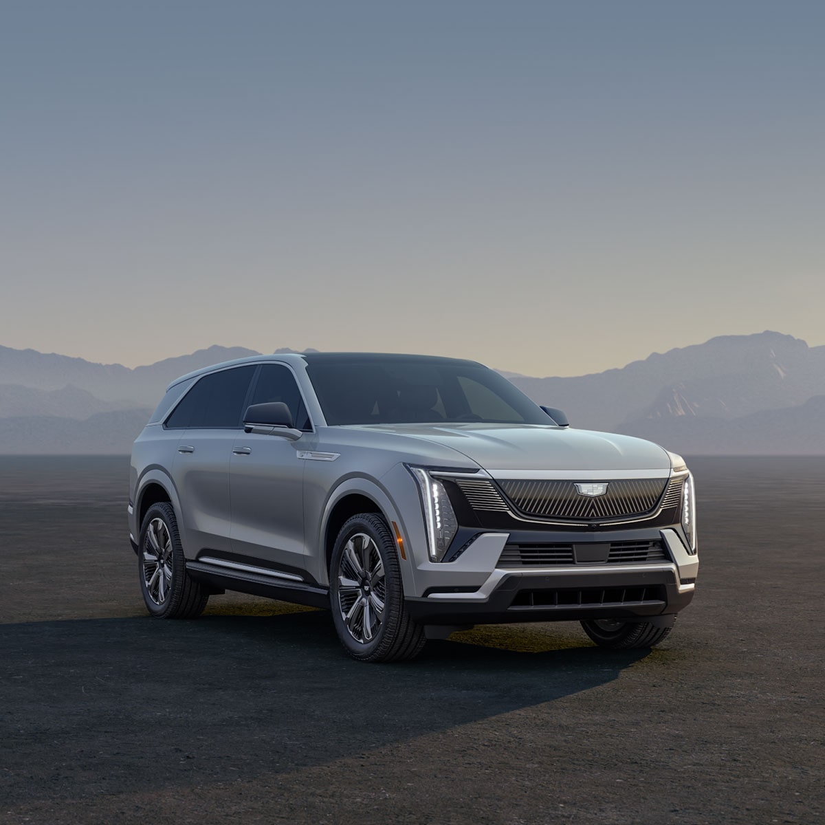 Three Cadillac Silver SUVs Parked on an Open Plain at Sunrise with  Mountains in the Background