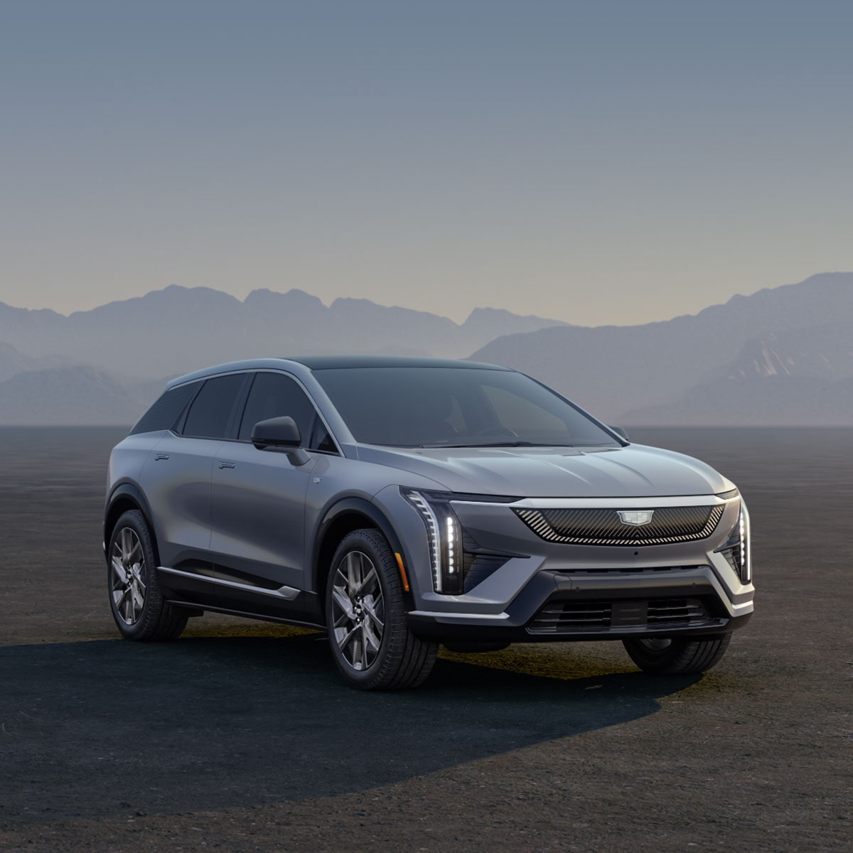 Three Cadillac Silver SUVs Parked on an Open Plain at Sunrise with  Mountains in the Background