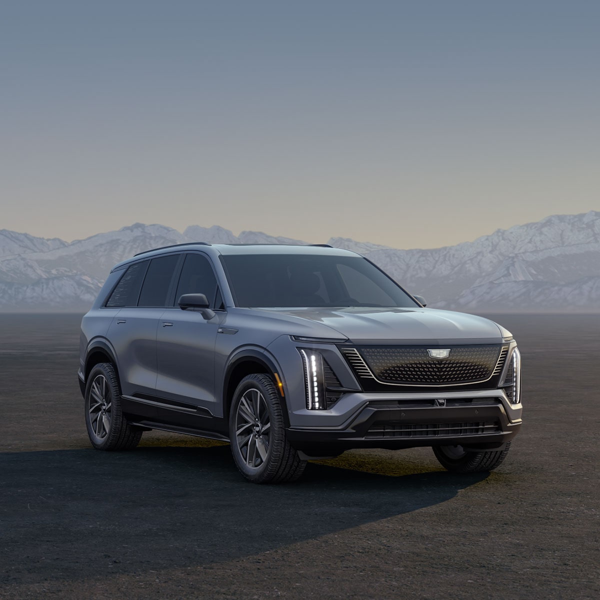 Three Cadillac Silver SUVs Parked on an Open Plain at Sunrise with  Mountains in the Background