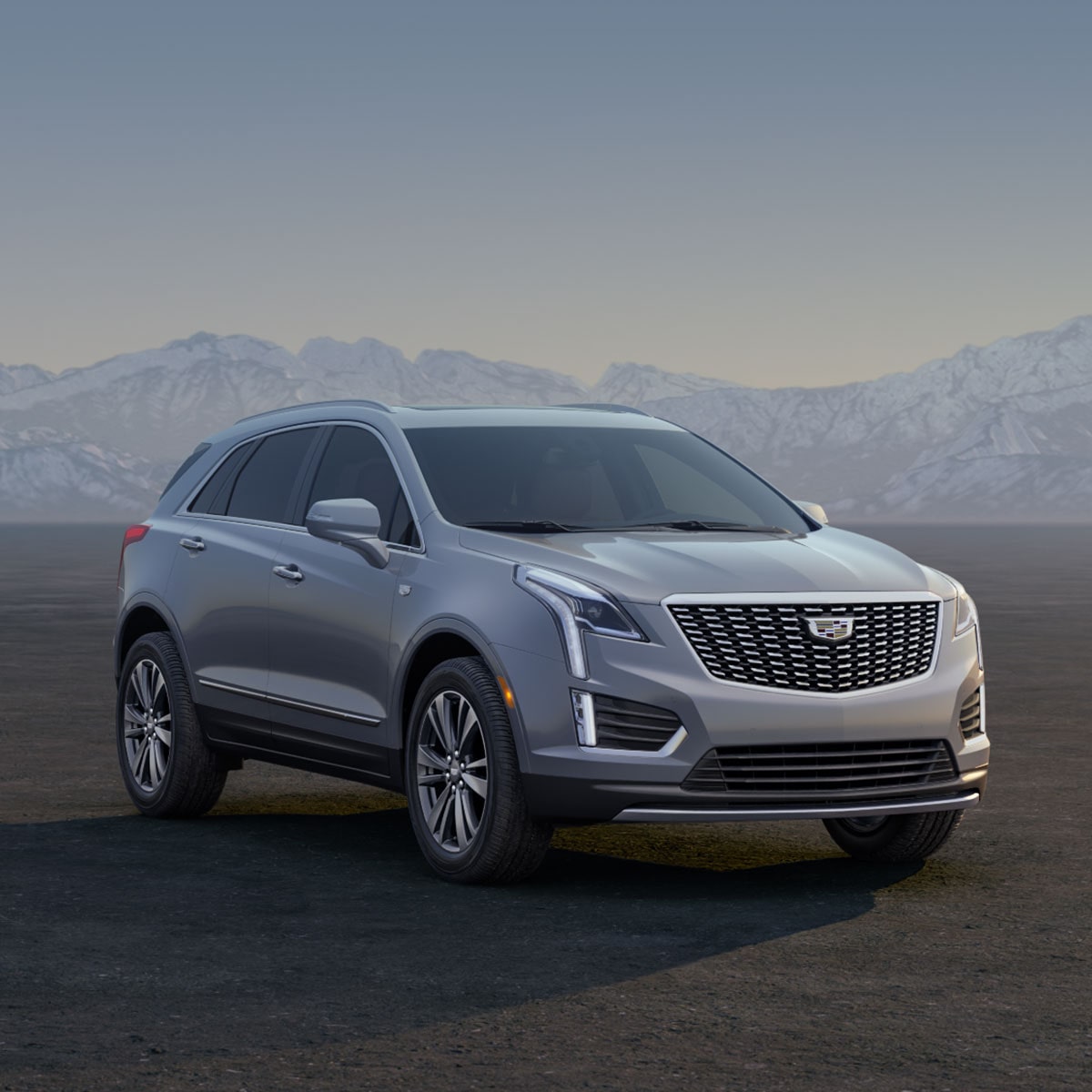 Three Cadillac Silver SUVs Parked on an Open Plain at Sunrise with  Mountains in the Background