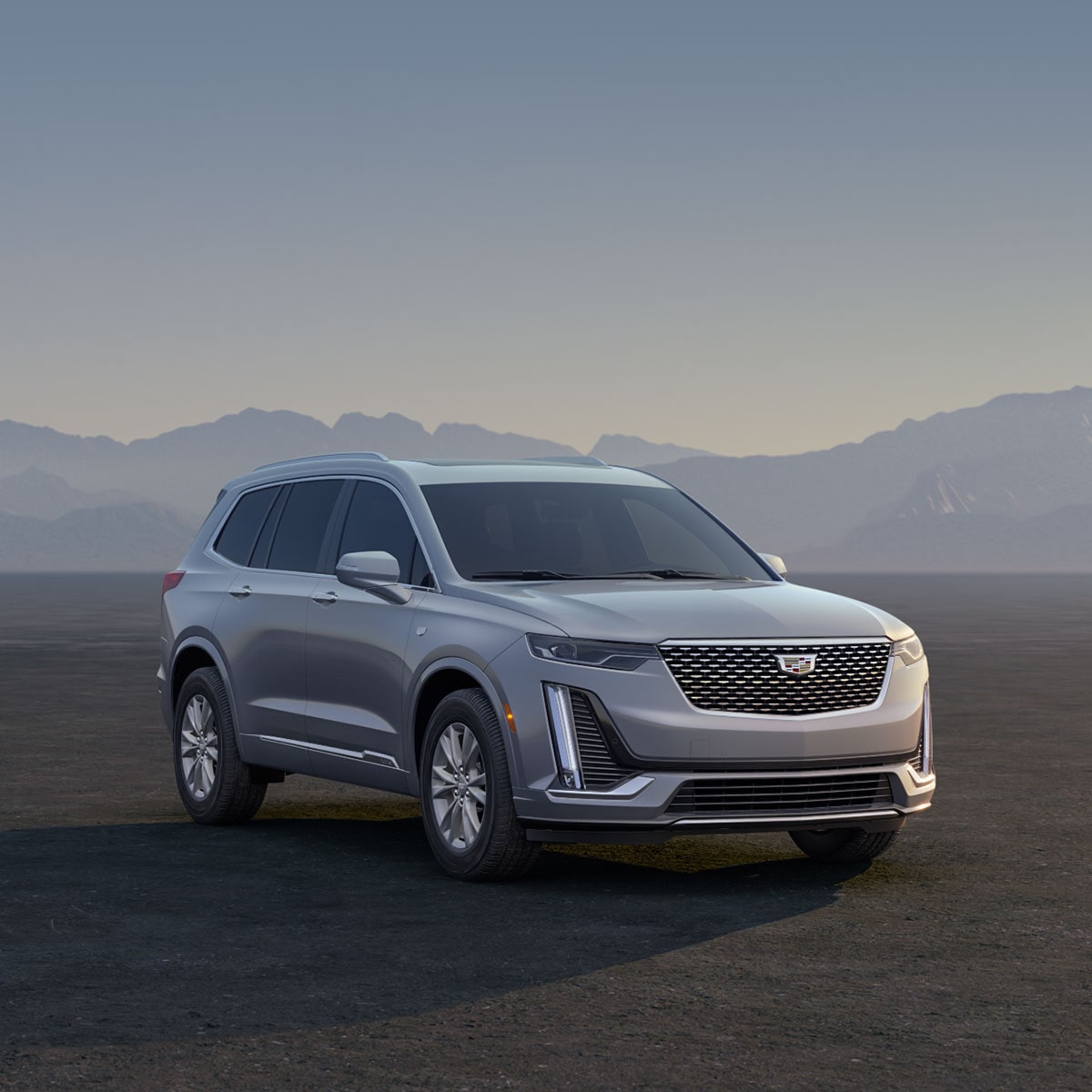 Three Cadillac Silver SUVs Parked on an Open Plain at Sunrise with  Mountains in the Background