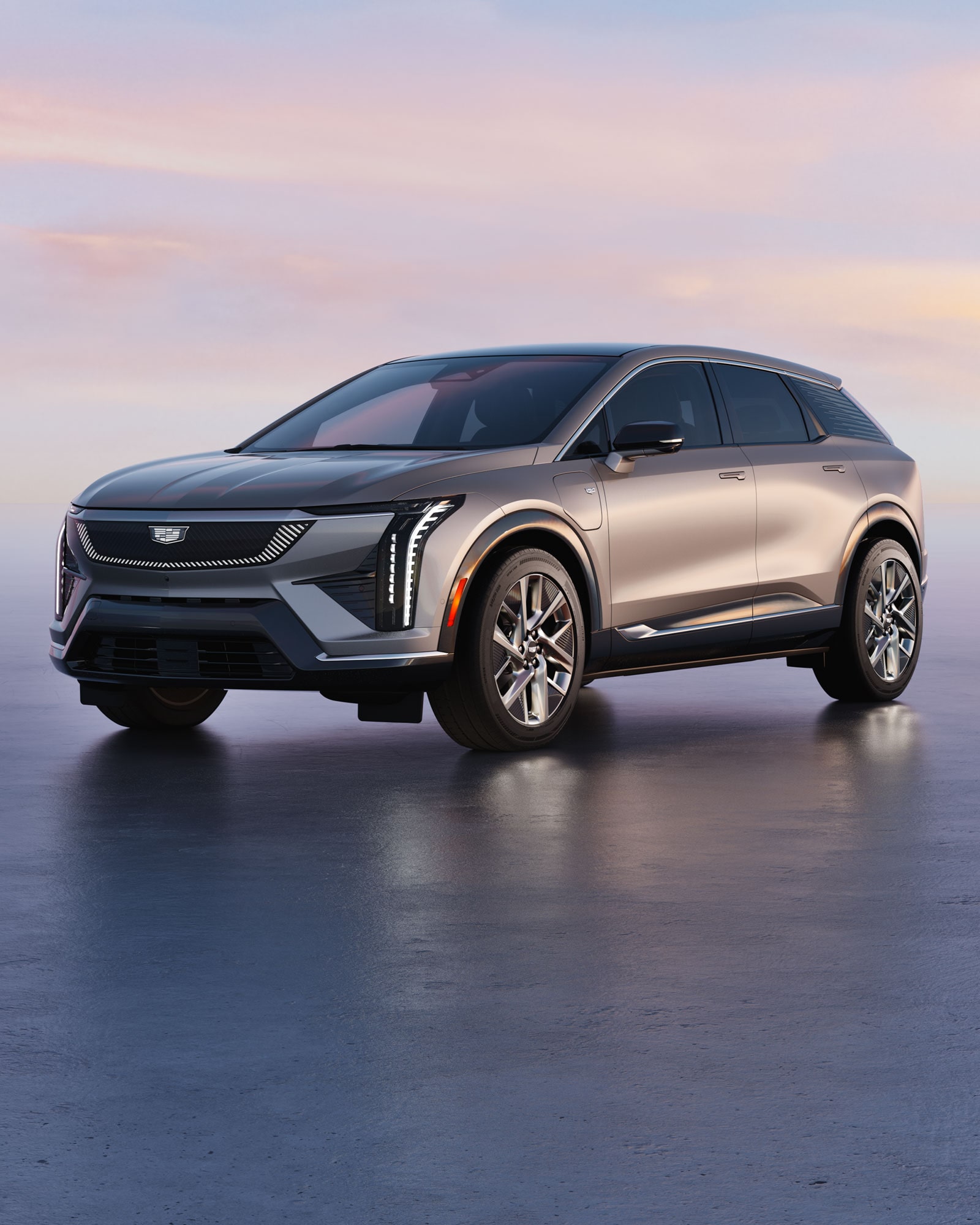 A multi-vehicle lineup of the Cadillac VISTIQ, LYRIQ, and OPTIQ parked on a paved stone driveway in front of a sunset