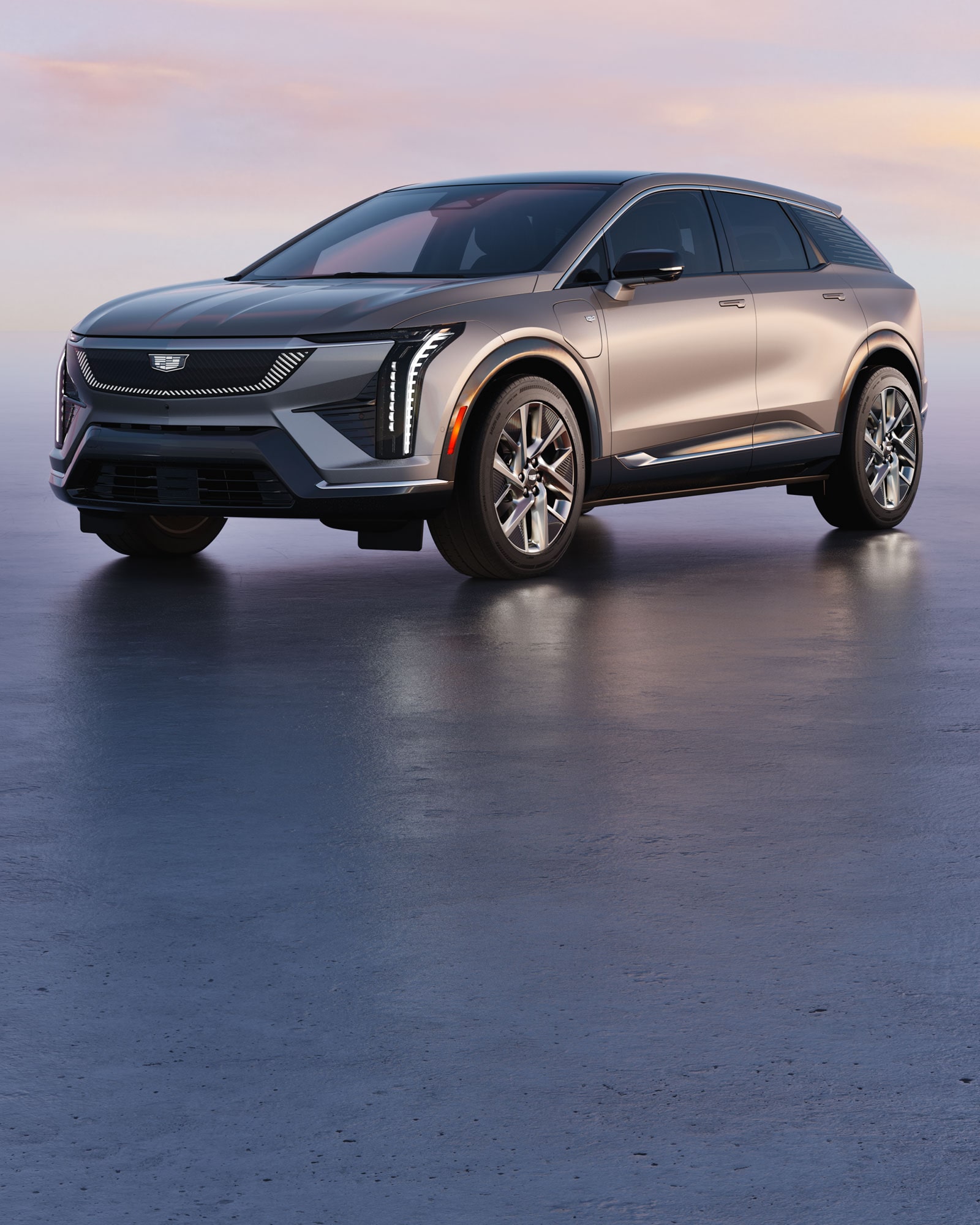 A multi-vehicle lineup of the Cadillac VISTIQ, LYRIQ, and OPTIQ parked on a paved stone driveway in front of a sunset