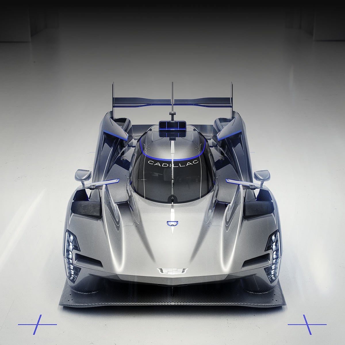 Front view of the Cadillac V-One Concept Race Car. The vehicle features a silver and dark blue aerodynamic body, enclosed cockpit canopy, prominent front fenders, and low-slung prototype racing design, centered against a light gray studio background