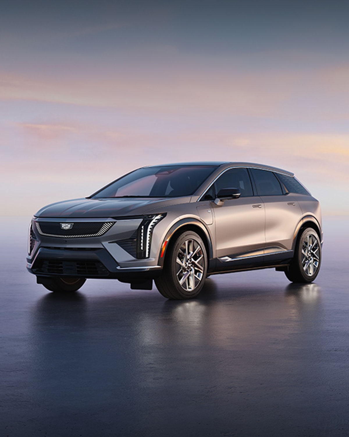 Image of a silver Cadillac OPTIQ electric SUV parked on a smooth, reflective surface at dusk, shown in a three-quarter front view. Large text reads “2025/2026 Cadillac OPTIQ Models,” “0.9% APR for 72 months,” and “$2,000 purchase allowance,” with fine-print offer details along the bottom.