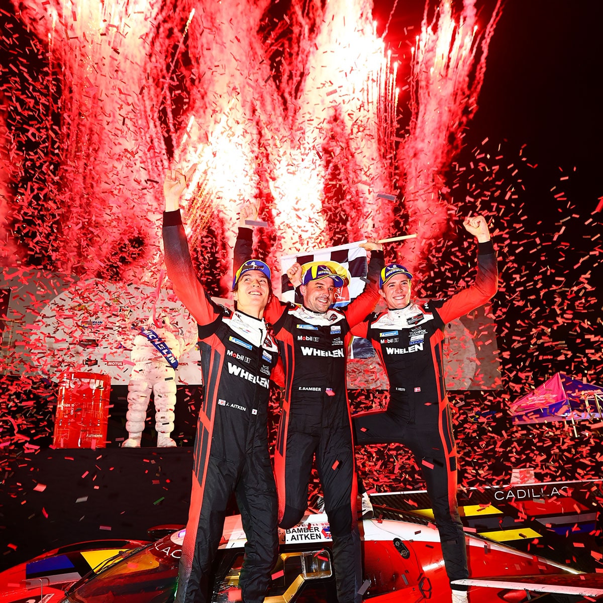 Front View of the Cadillac Racing Team Celebrating Their Win and Red Fireworks Going Off Behind Them