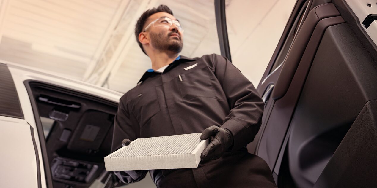 Técnico de Cadillac sosteniendo un filtro de aire de cabina junto a un vehículo