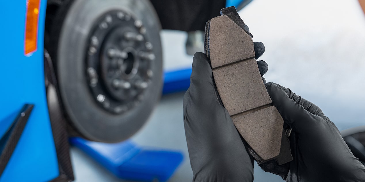 A View of a Mechanic Holding a Break Pad in Front of an Exposed Wheel