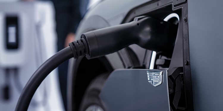 Primer plano de un cargador enchufado en el puerto de carga de un vehículo eléctrico Cadillac