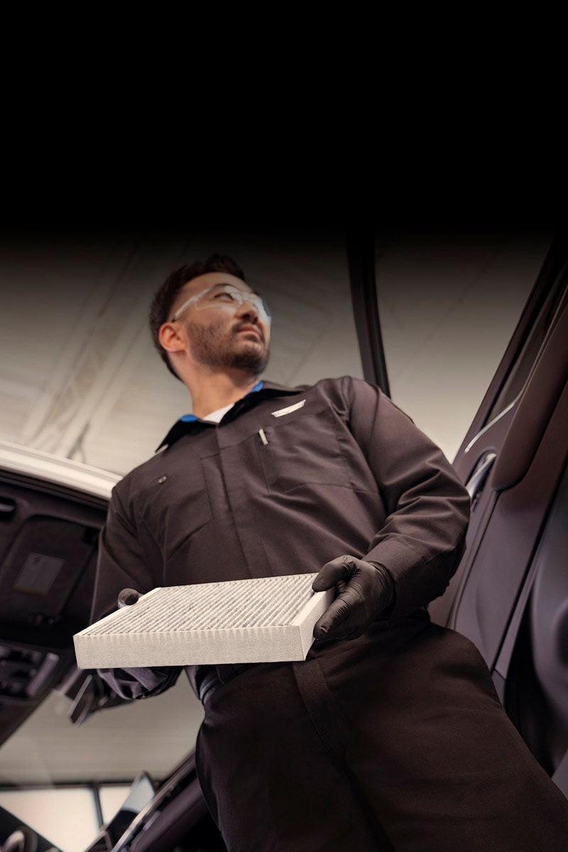 Técnico de servicio certificado de Cadillac sosteniendo el filtro de aire de la cabina de un vehículo