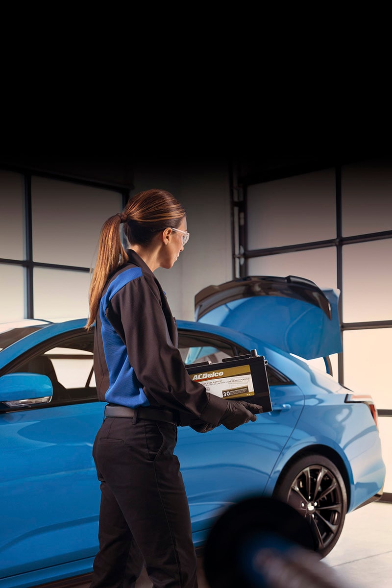 Técnica de servicio certificado de Cadillac llevando una batería ACDelco Gold para instalarla en un vehículo