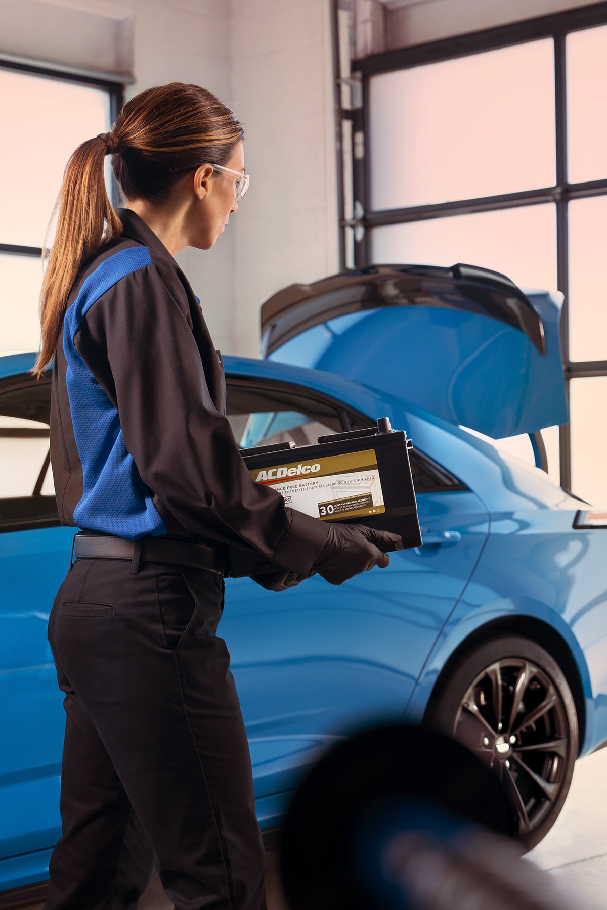 Técnica de servicio certificado de Cadillac llevando una batería ACDelco Gold para instalarla en un vehículo