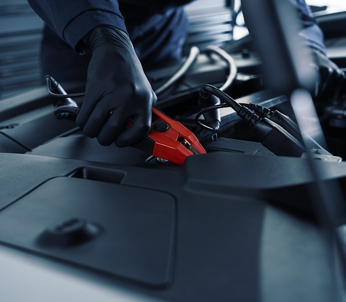 Técnico de servicio certificado de Cadillac conectando cables para puentear baterías en un vehículo