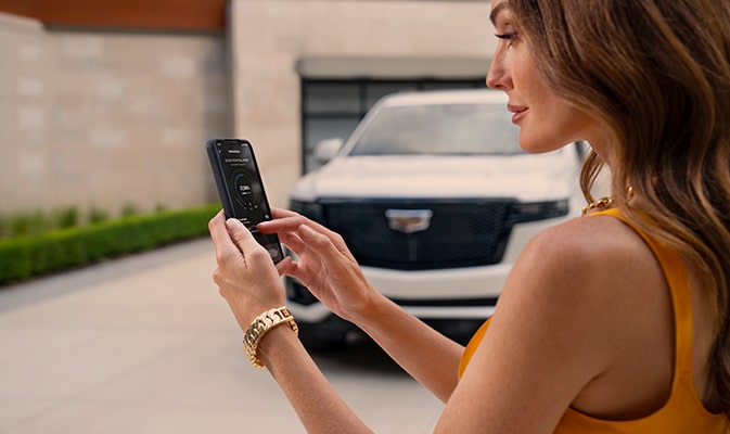 Una mujer usa la aplicación móvil Cadillac en su smartphone de pie junto a su vehículo Cadillac
