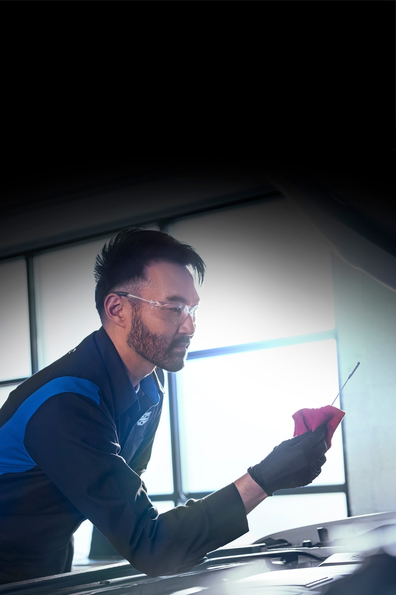 Técnico de servicio certificado de Cadillac verificando el nivel de aceite del vehículo con una varilla de medición