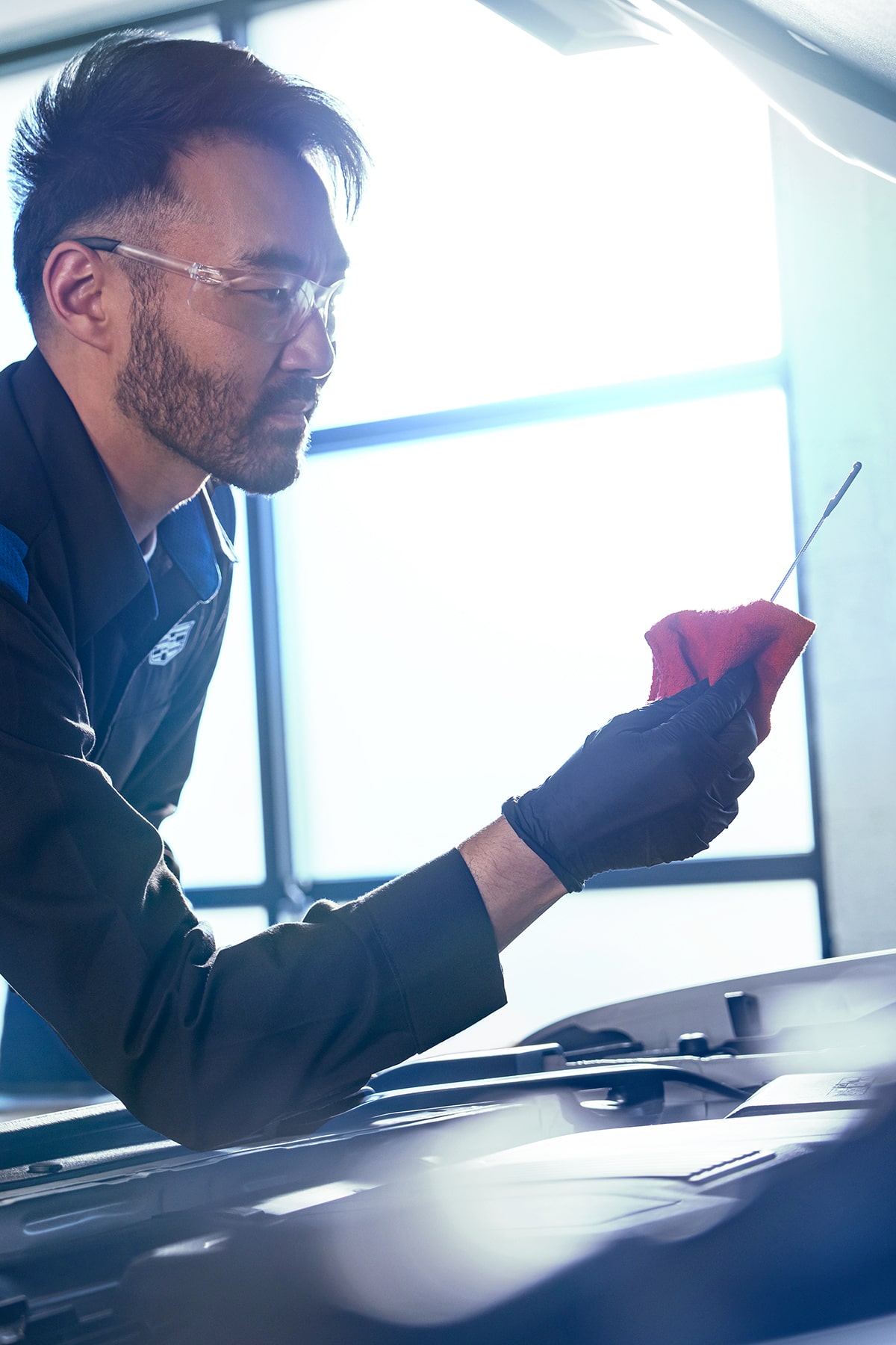 Técnico de servicio certificado de Cadillac verificando el nivel de aceite del vehículo con una varilla de medición