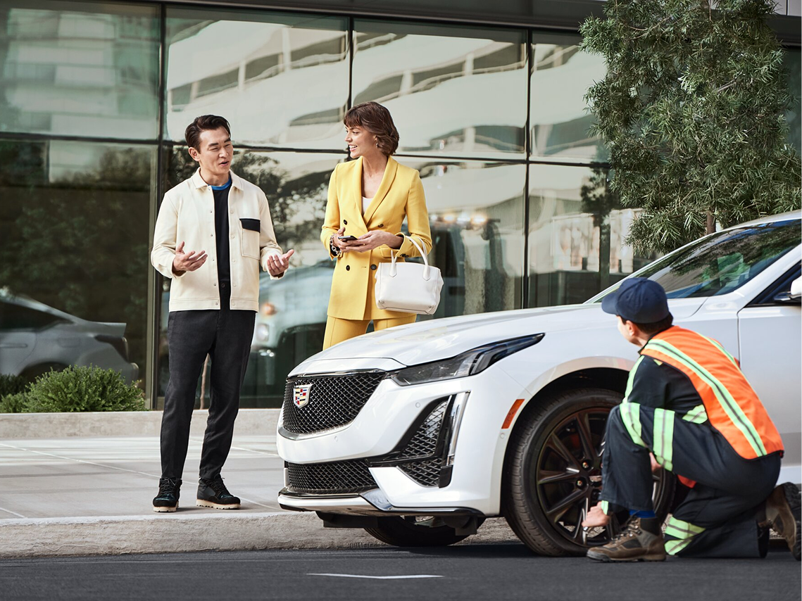 A Woman Talking with an OnStar Advisor While Her Cadillac's Tire is Checked by Service Team