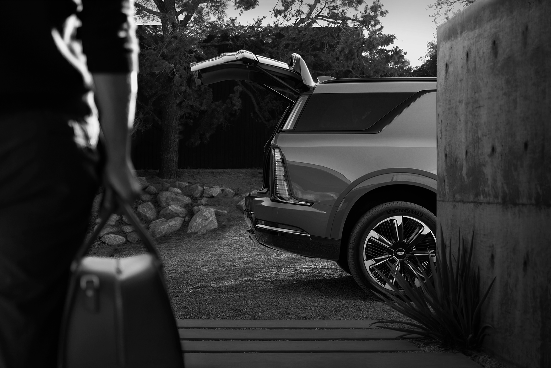 Black and White View of the Rear of a Cadillac Escalade with its Trunk Open and a Person with a Bag