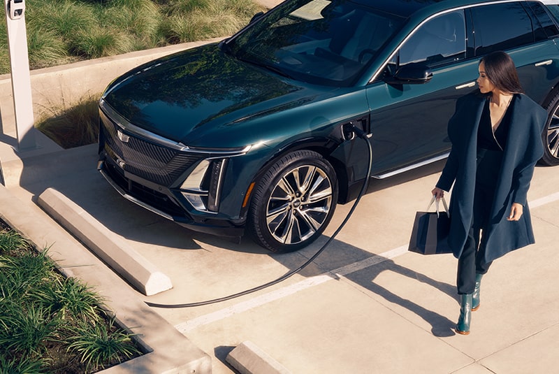 An Overview Shot View of a Woman Looking at a Cadillac EV Being Charged